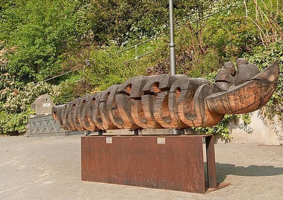 Zwei Personen auf einer Bank neben einer großen Holzskulptur in der Natur