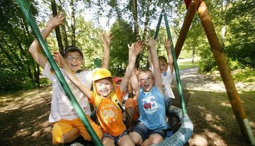Sechs Kinder genießen das Spielen auf einer Schaukel im Freien.