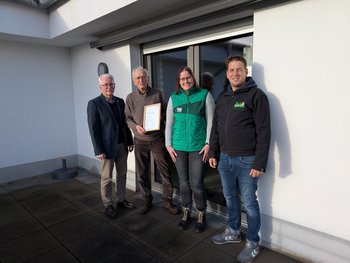 Vier Personen stehen auf einer Terrasse mit einer Urkunde.