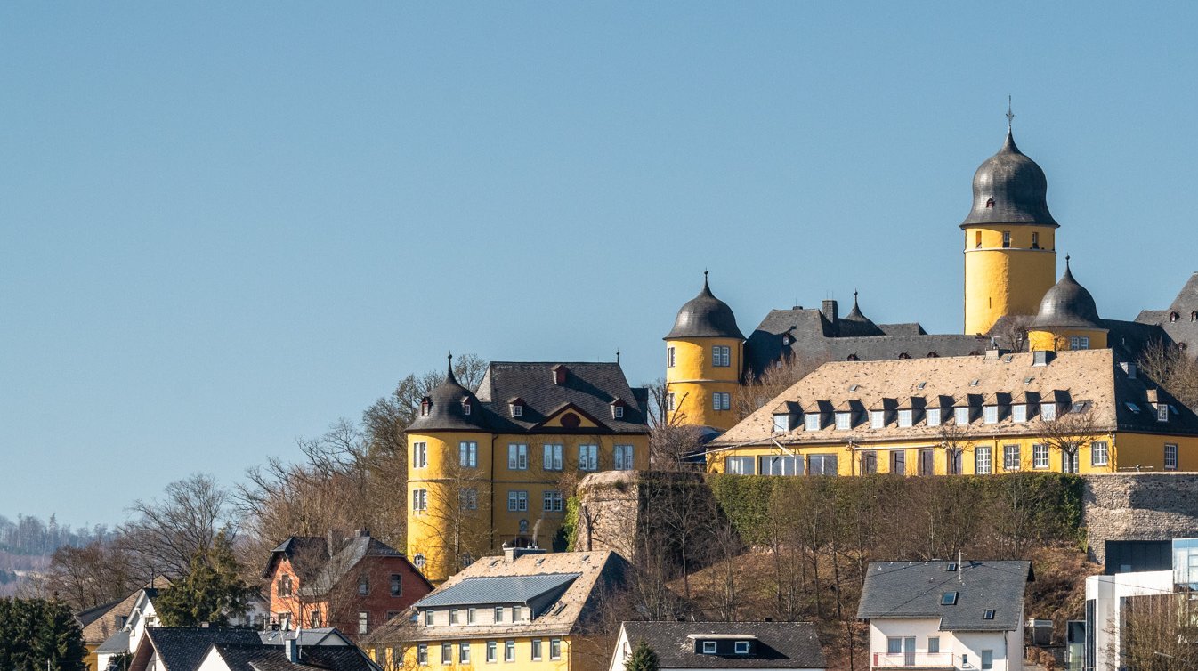 Eine Burg thront über einer Stadt mit gewöhnlicher Architektur im Vordergrund.